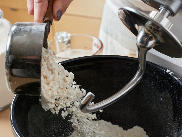 Person pouring flour into a KitchenAid® Stand Mixer with Dough Hook Attachment