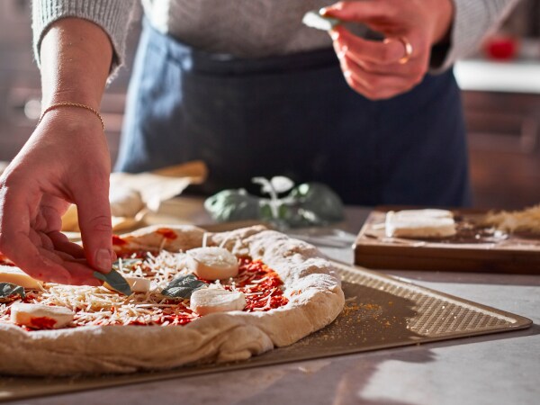 Person adding toppings to a pizza