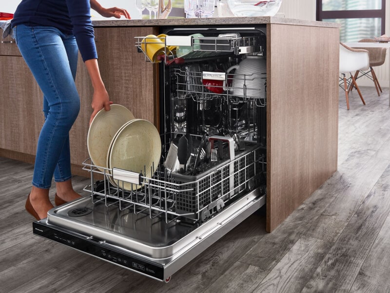 A woman placing a plate in a dishwasher A woman placing a plate in a dishwasher