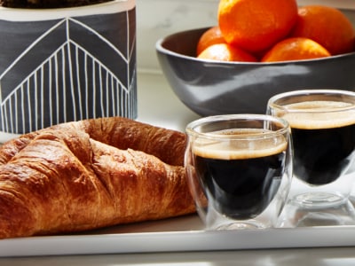 Croissants and cups of espresso on a tray in front of a bowl of oranges. Croissants and cups of espresso on a tray in front of a bowl of oranges.