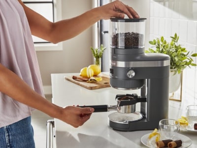 Hand placing portafilter under burr coffee grinder. Hand placing portafilter under burr coffee grinder.