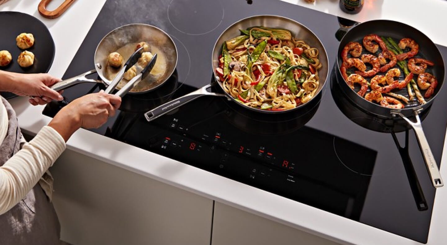 A person cooking pasta and shrimp on a black KitchenAid® electric induction cooktop A person cooking pasta and shrimp on a black KitchenAid® electric induction cooktop
