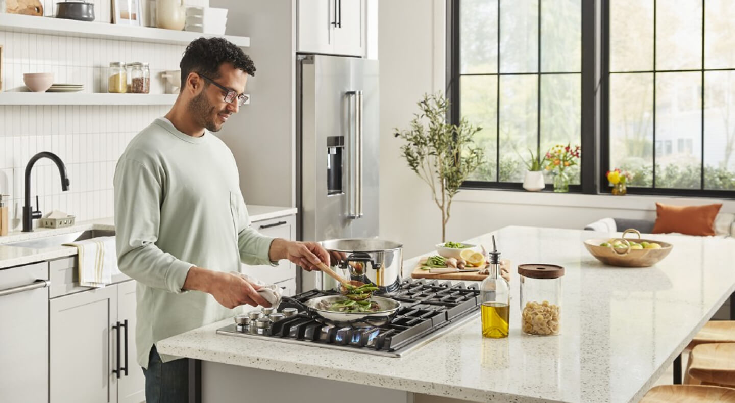 A person cooking food on a KitchenAid® gas cooktop in a modern kitchen