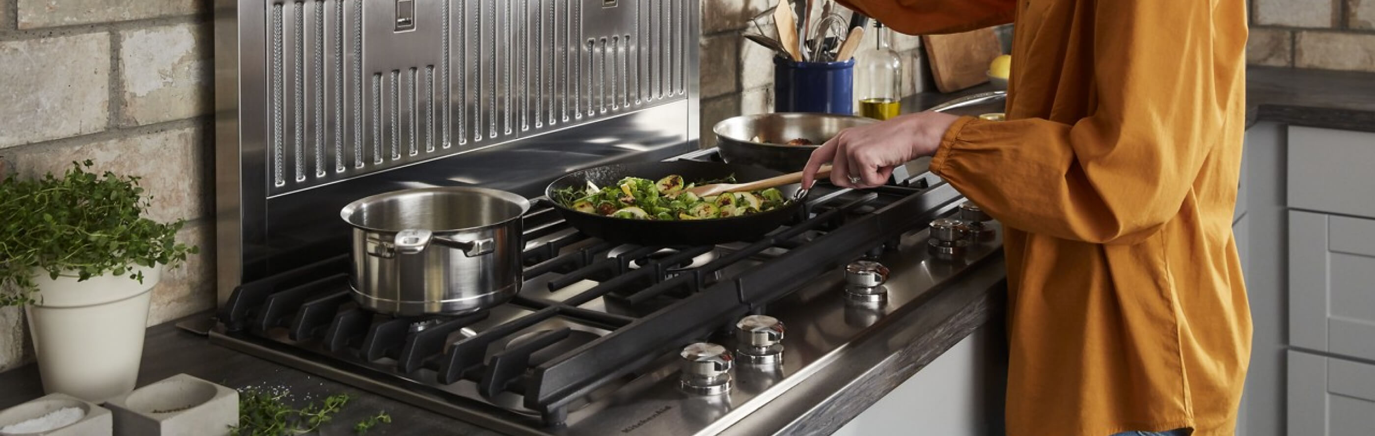 A closeup of a KitchenAid® gas cooktop with a person cooking food 