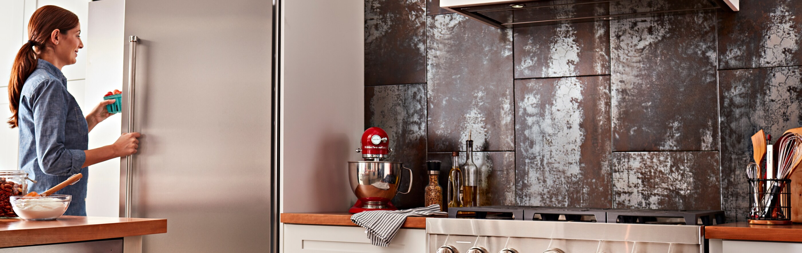 Woman opening a built-in side-by-side refrigerator in a kitchen with commercial-style appliances