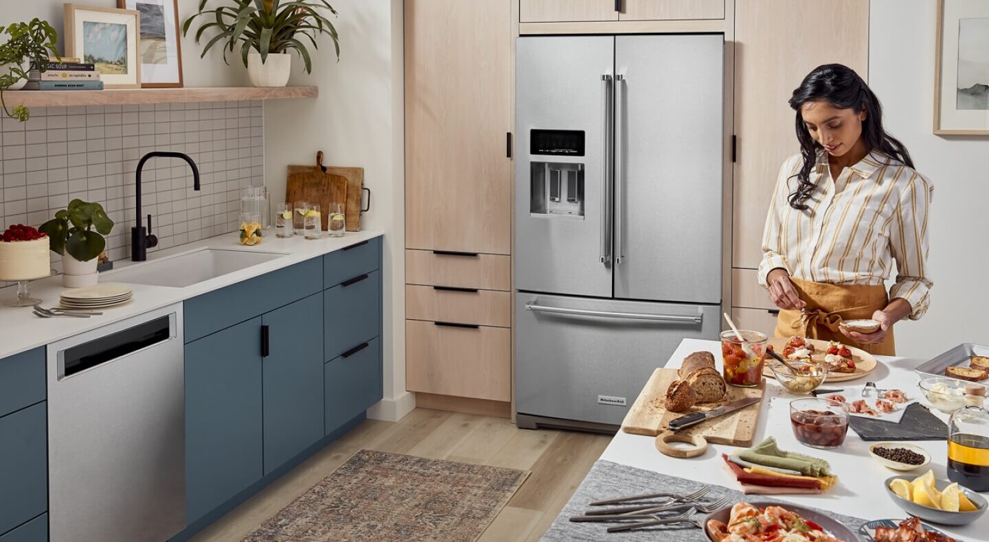 A woman preparing food at her kitchen island with a French door refrigerator in the background