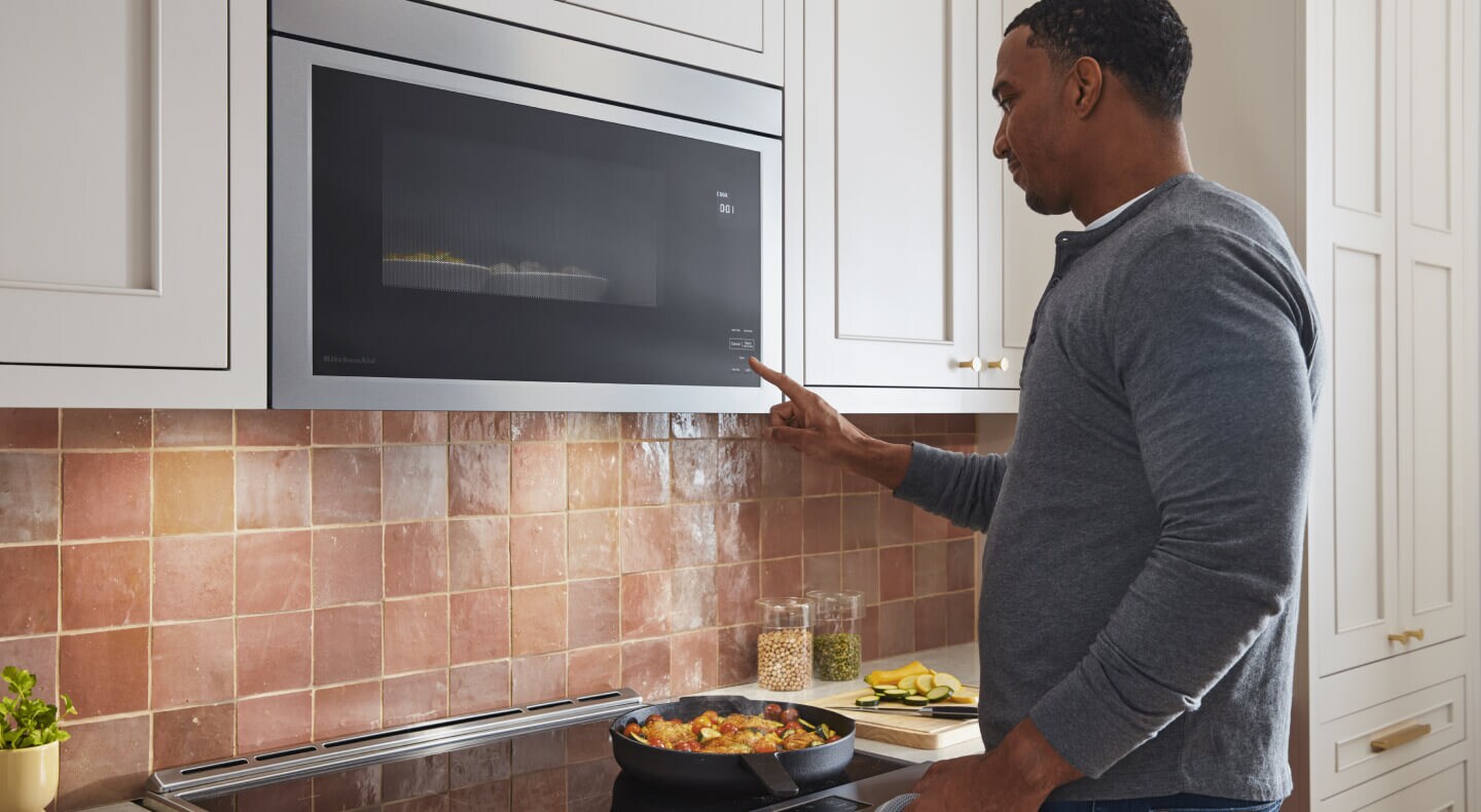 A person selecting a microwave setting on an over-the-range KitchenAid® microwave