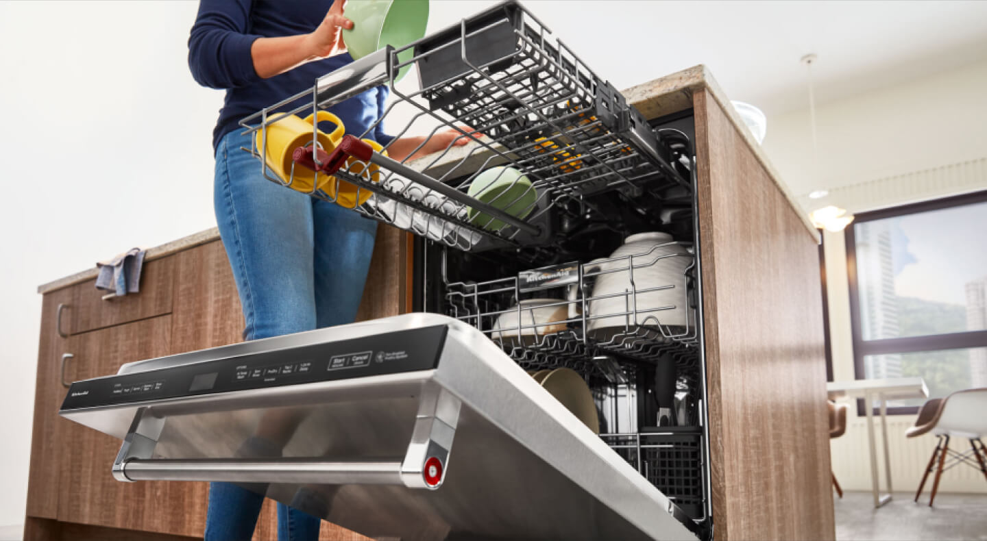 Person loading the top third rack of a dishwasher with a green bowl