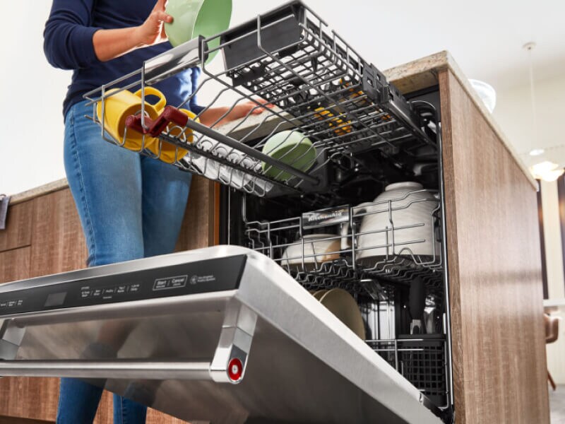 Person loading the top third rack of a dishwasher with a green bowl