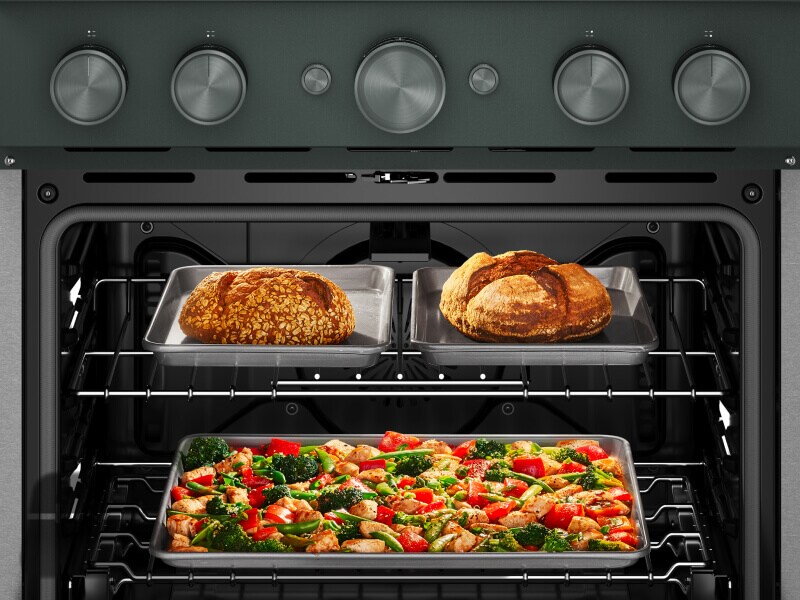 An open range with two loaves of bread on the top rack and a vegetable and chicken dish on the bottom rack