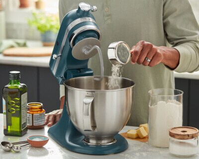 Person adding ingredients to a stand mixer bowl
