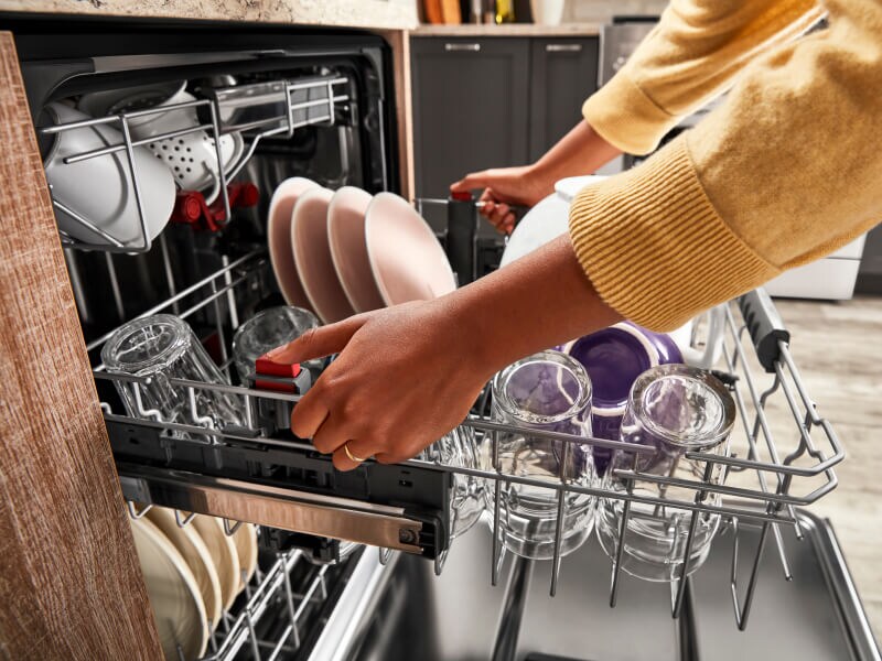 Person pulling out a dishwasher rack filled with cups and plates Person pulling out a dishwasher rack filled with cups and plates