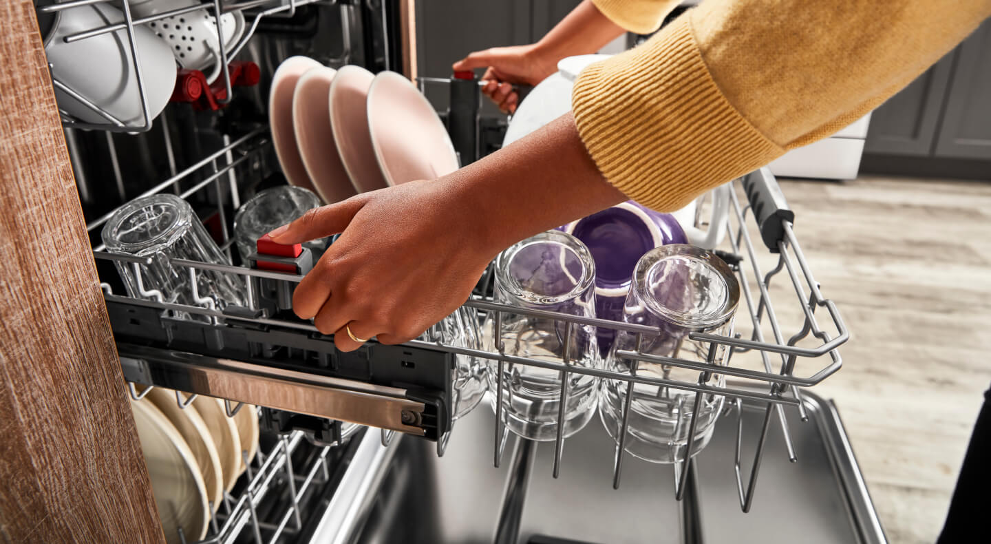 Person pulling out a dishwasher rack filled with cups and plates Person pulling out a dishwasher rack filled with cups and plates