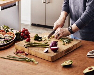 A person chopping onions, asparagus and other vegetables on a kitchen island