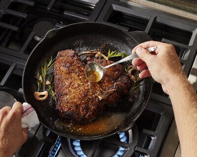 A person basting a steak cooking in a cast-iron skillet