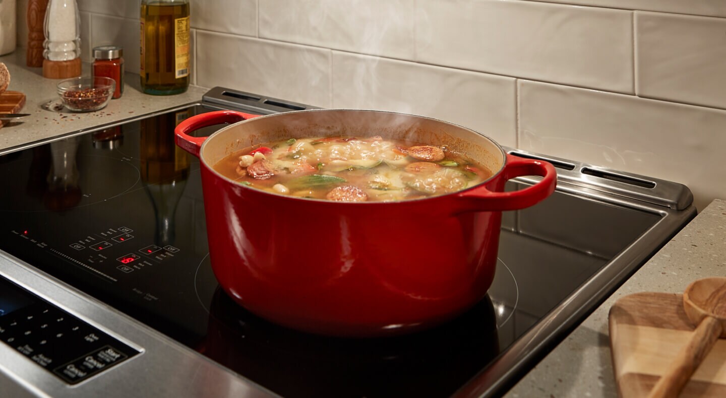 A sausage-based stew cooking in a red Dutch oven on a stovetop A sausage-based stew cooking in a red Dutch oven on a stovetop