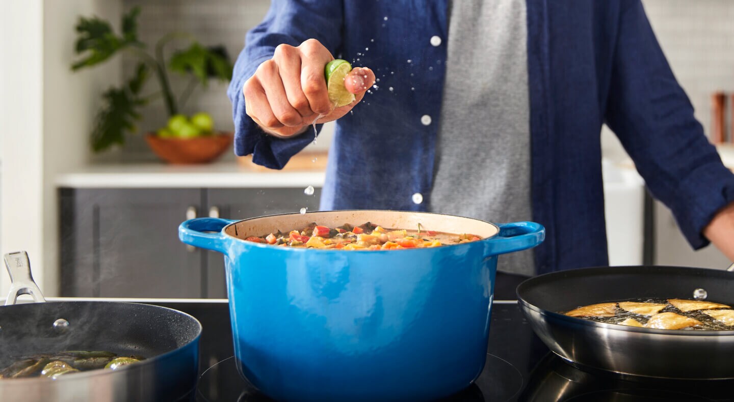 A person squeezing a lime over a rich stew cooking in a blue Dutch oven A person squeezing a lime over a rich stew cooking in a blue Dutch oven
