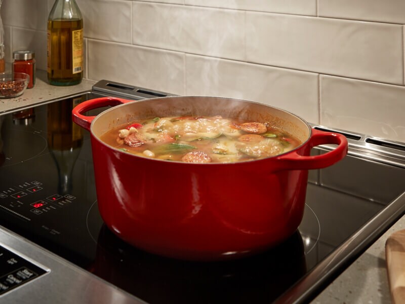 A sausage-based stew cooking in a red Dutch oven on a stovetop A sausage-based stew cooking in a red Dutch oven on a stovetop