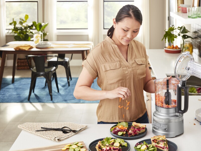 Woman placing carrots grated in KitchenAid® food processor on salad Woman placing carrots grated in KitchenAid® food processor on salad