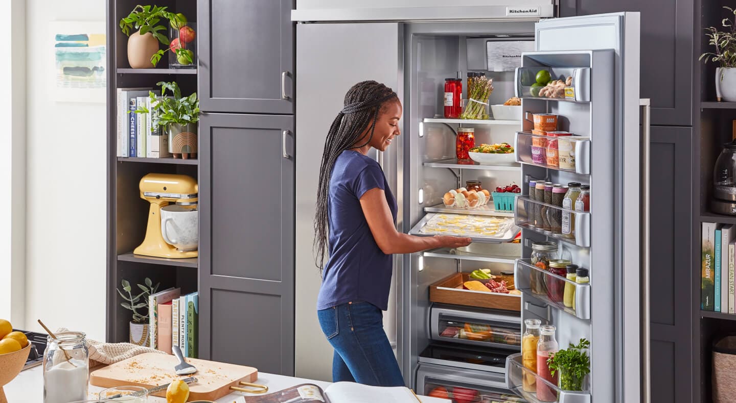 A woman in her kitchen, standing in front of a KitchenAid® built-in refrigerator