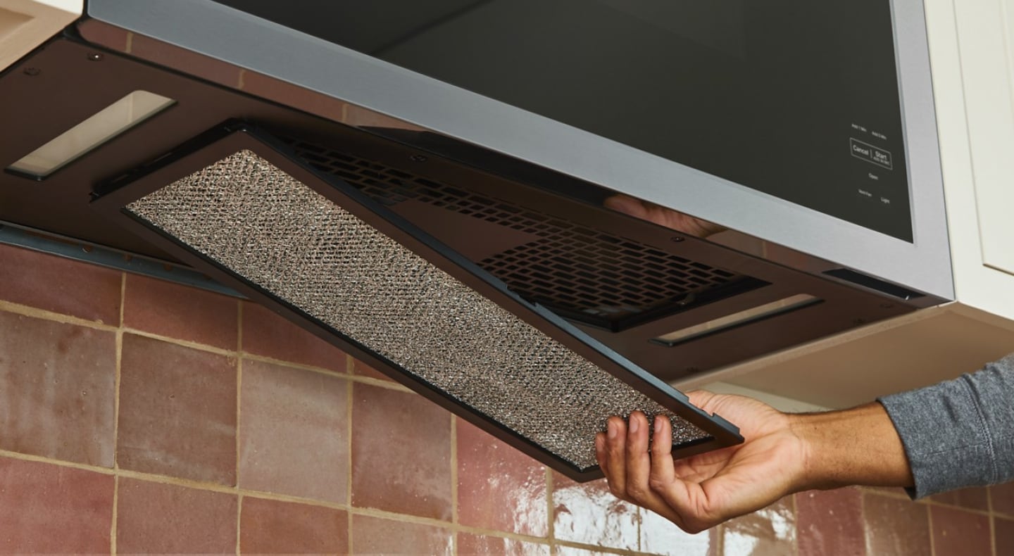 Close-up of person removing the filter from an over-the-range microwave vent Close-up of person removing the filter from an over-the-range microwave vent