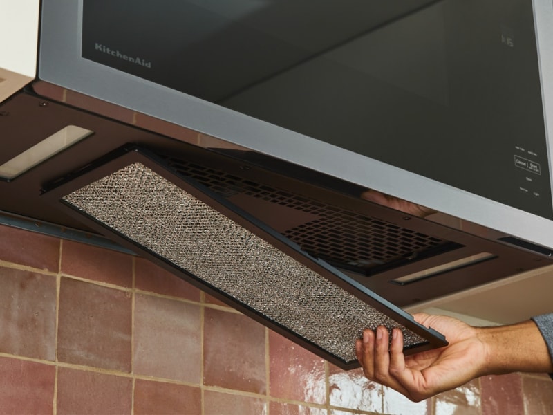 Close-up of person removing the filter from an over-the-range microwave vent Close-up of person removing the filter from an over-the-range microwave vent