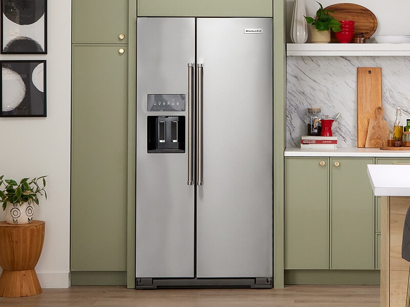 A KitchenAid® side-by-side refrigerator within muted green cabinets