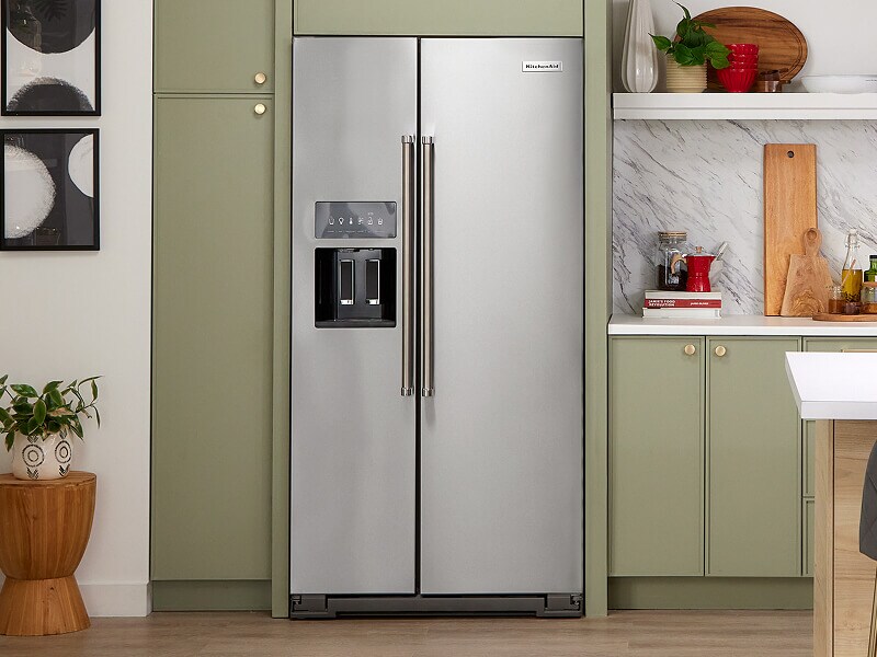A KitchenAid® side-by-side refrigerator within muted green cabinets