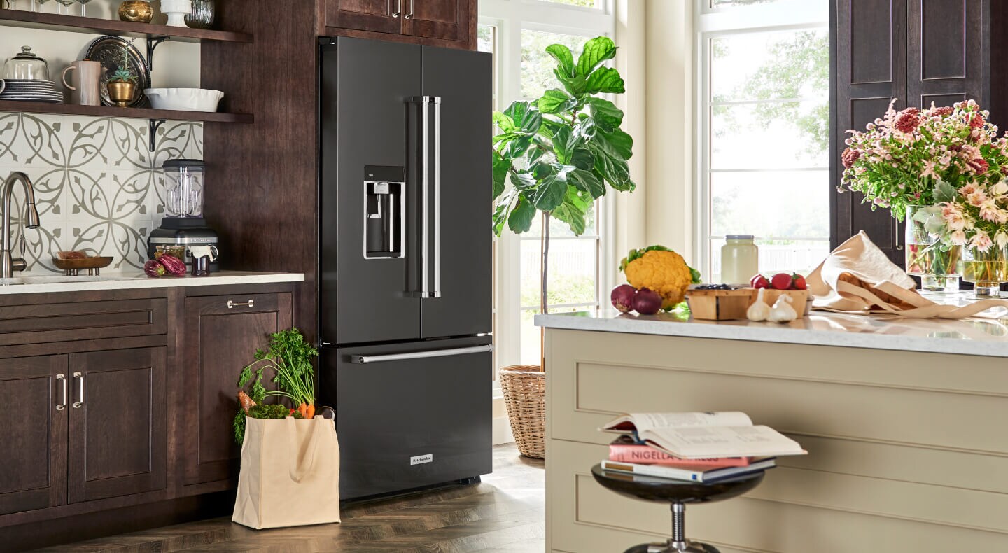 A black stainless steel KitchenAid® French door refrigerator with a bag of fresh produce beside it A black stainless steel KitchenAid® French door refrigerator with a bag of fresh produce beside it