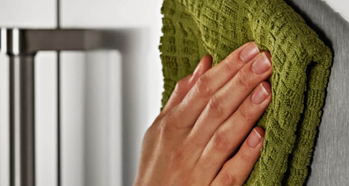 A person using a soft cloth to wipe the exterior of the KitchenAid® French Door Bottom Mount Refrigerator.