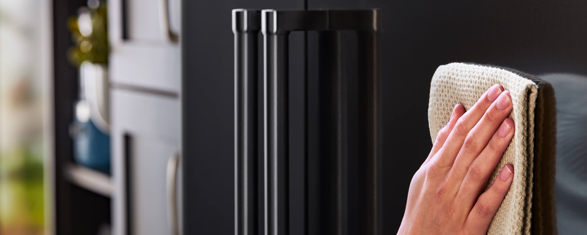 A person using a soft cloth to wipe the exterior of the KitchenAid® French Door Bottom Mount Refrigerator.