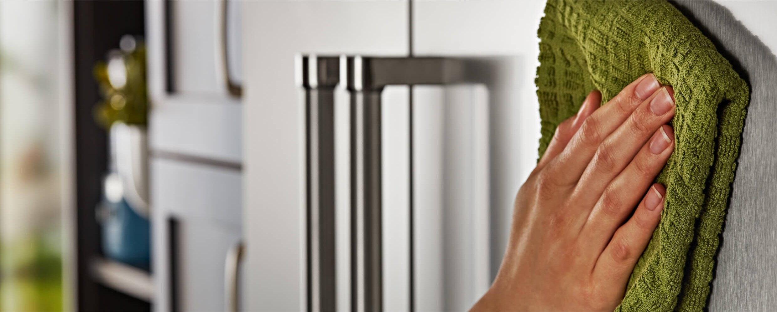 A person using a soft cloth to wipe the exterior of the KitchenAid® French Door Bottom Mount Refrigerator.