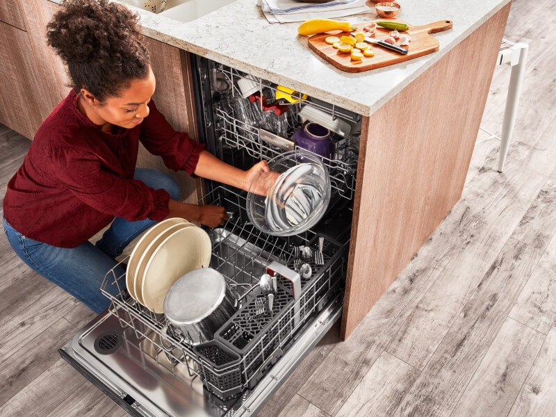 Person loading a glass mixing bowl into the bottom rack of a dishwasher Person loading a glass mixing bowl into the bottom rack of a dishwasher