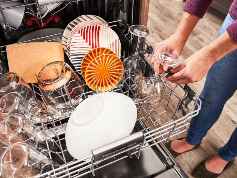 Person loading wine glasses in the top rack of a dishwasher Person loading wine glasses in the top rack of a dishwasher