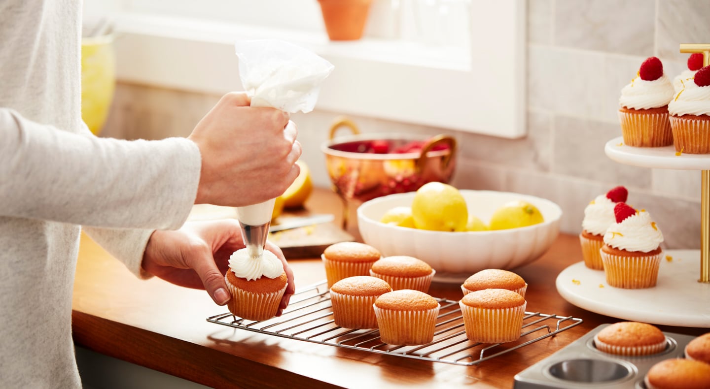 Person decorating cupcakes with vanilla buttercream frosting Person decorating cupcakes with vanilla buttercream frosting