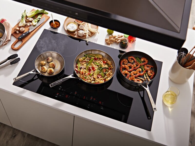 Three pans with food in them cooking on an induction cooktop