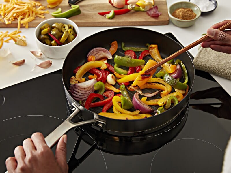 Person stirring vegetables in a pan on a cooktop