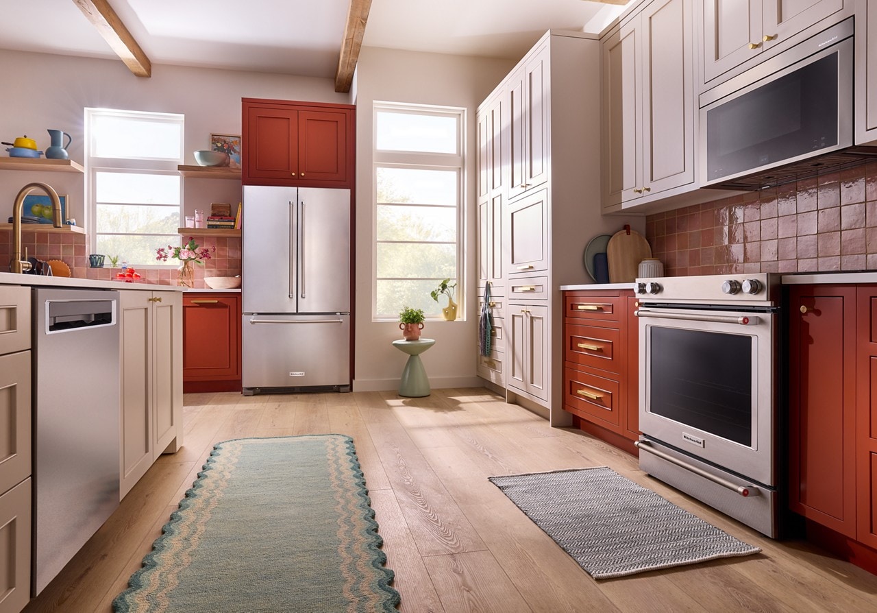 A suite of KitchenAidÂŽ stainless steel appliances in a burnt orange kitchen