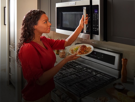 Woman holding food with her hand on microwave door.