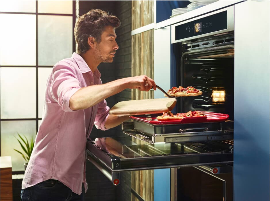 A man gently removing his freshly baked flatbread pizzas from his oven.