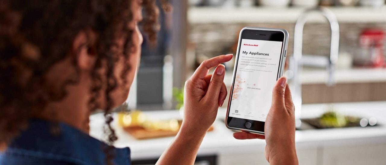 A woman using the KitchenAid™ app on her smartphone to add her connected appliances. A woman using the KitchenAid™ app on her smartphone to add her connected appliances.