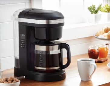 KitchenAid® Drip Coffee Maker with white coffee cup and sugar on countertop.