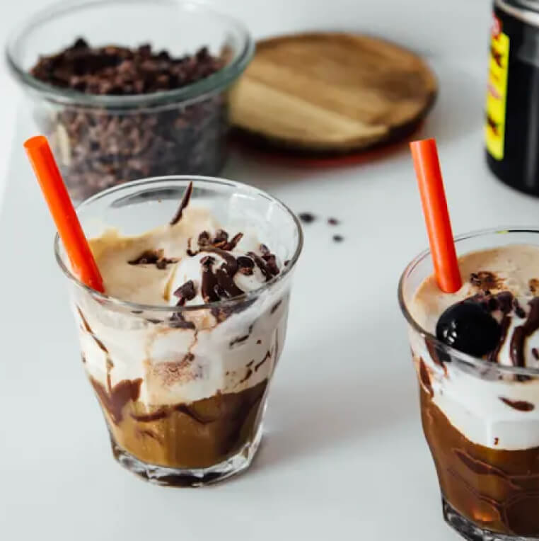 Two cups of cold brew coffee floats with a glass container of coffee beans in the background. Two cups of cold brew coffee floats with a glass container of coffee beans in the background.