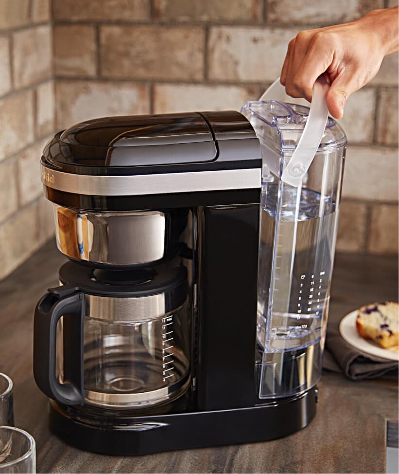 Hand removing water reservoir from base of KitchenAid® Drip Coffee maker.