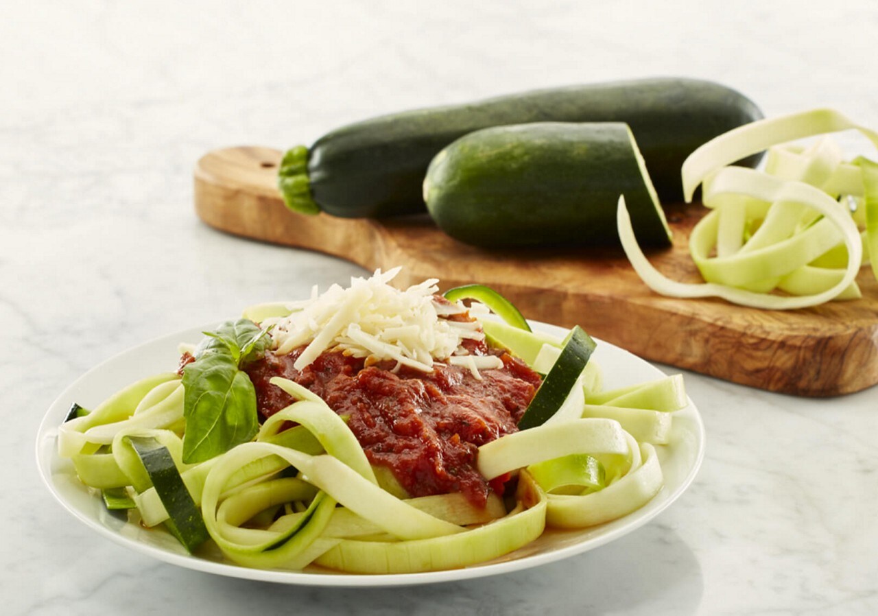 Zucchini noodles in white bowl with red sauce and grated parmesan. Zucchini noodles in white bowl with red sauce and grated parmesan.