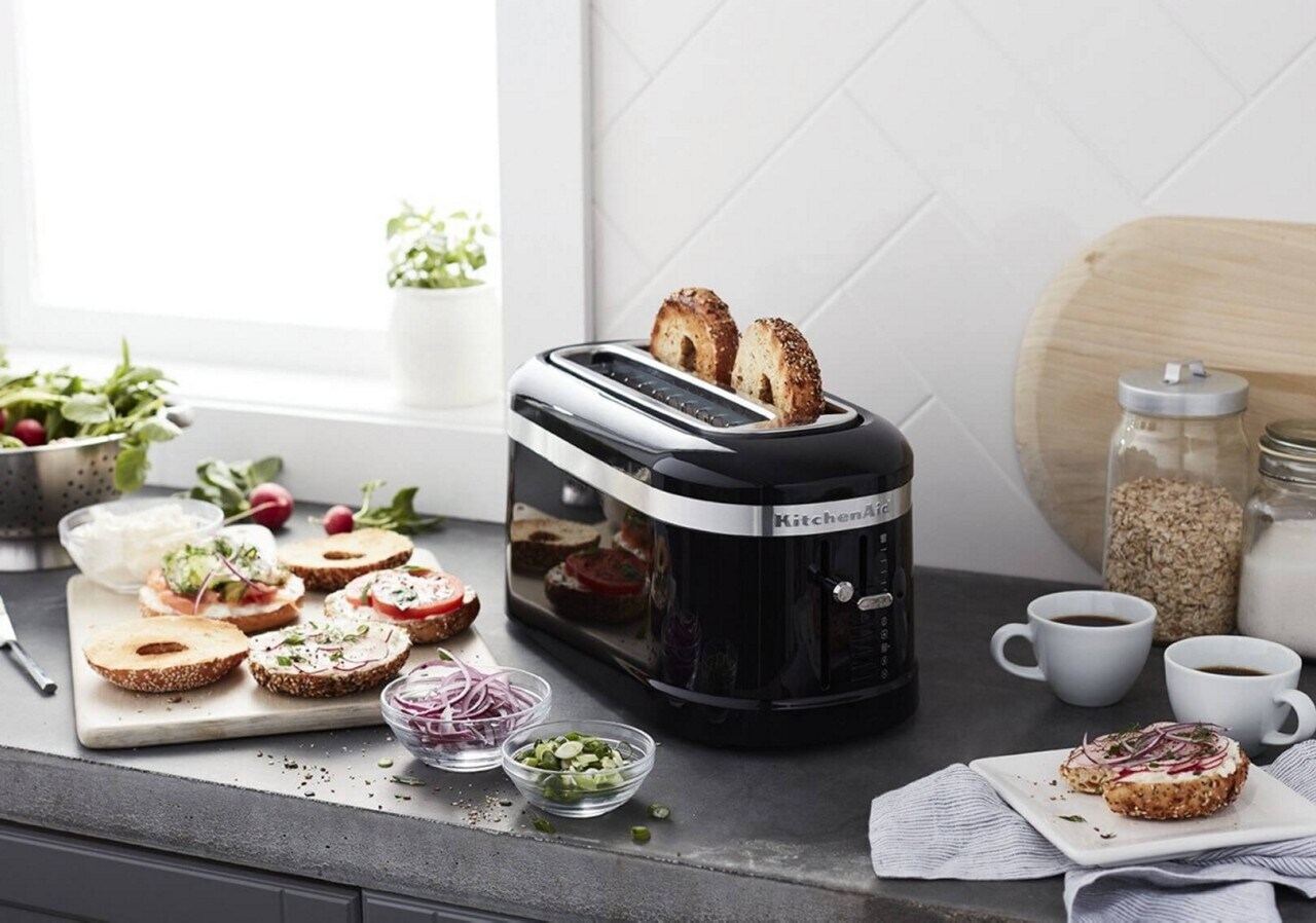 Black toaster on a counter with bagel and lox ingredients surrounding it Black toaster on a counter with bagel and lox ingredients surrounding it