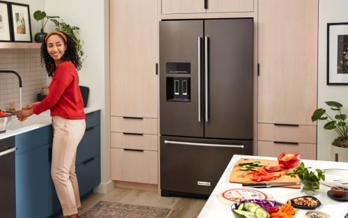 Person washing vegetables at a sink with a KitchenAid® refrigerator in the background