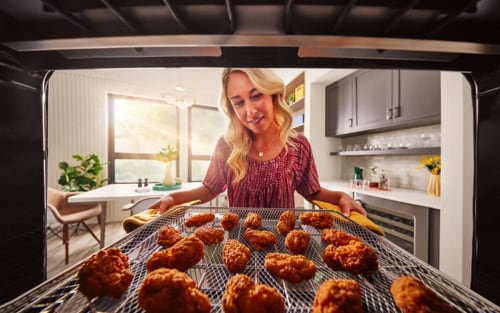 A woman holds a metal air fryer basket full of breaded pieces of chicken