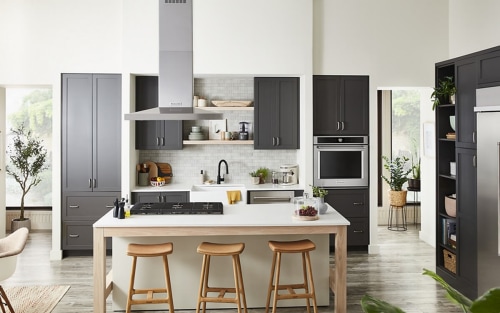 A long and narrow kitchen with brown cabinets and white cabinets against the wall with a white island in the middle of the room