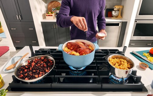 A person preparing three dishes on a gas stove